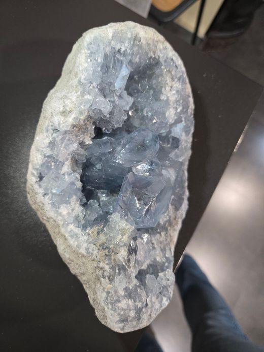 Géode de cristal à centre creux, posée verticalement sur une table sombre.