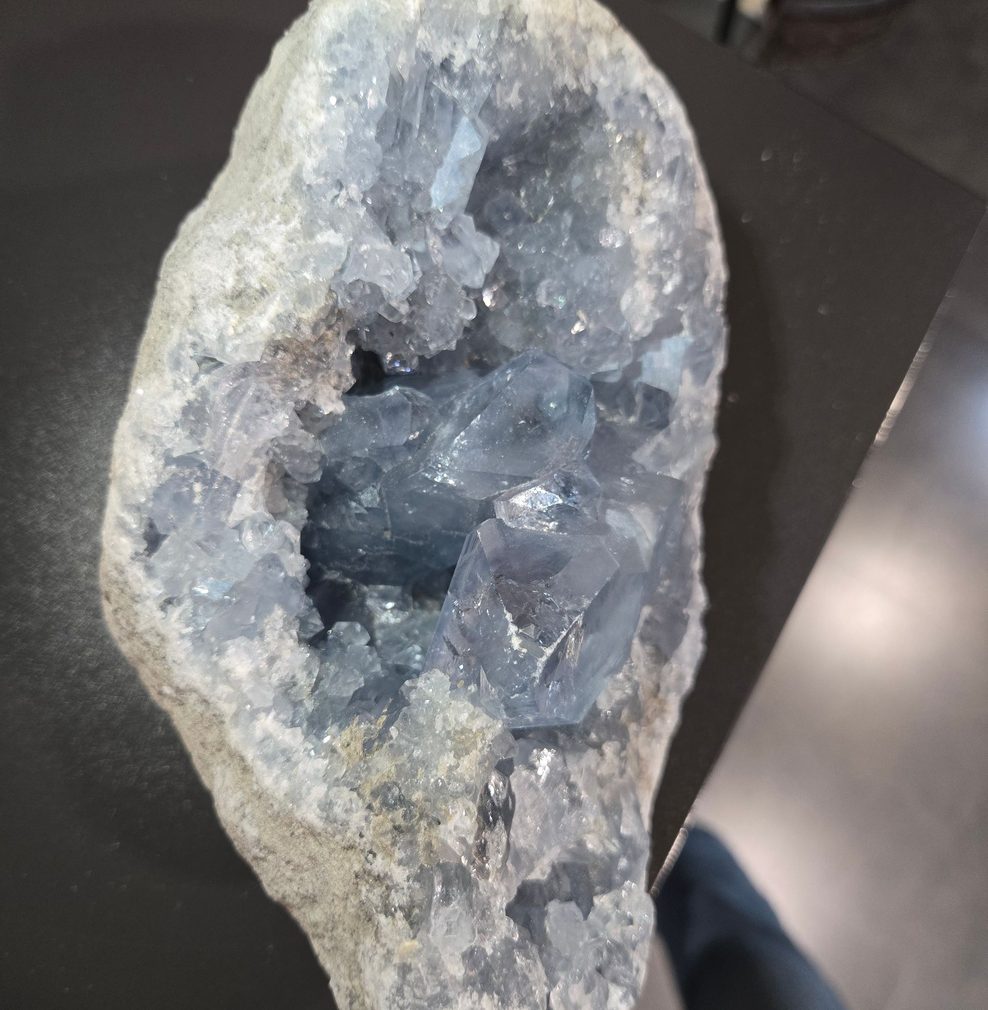 Géode en cristal avec un centre creux posée sur une table sombre.