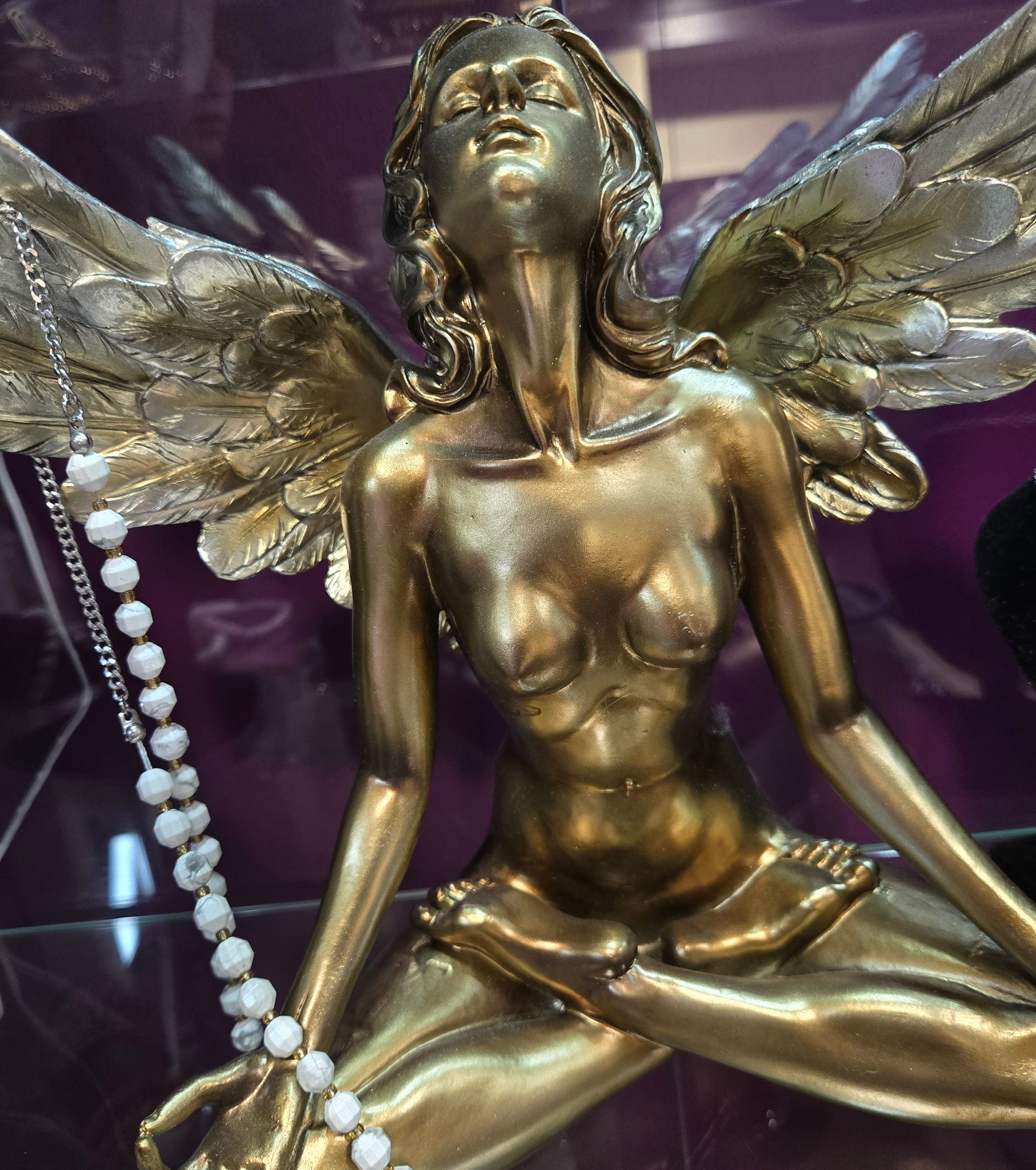 Statue de fée ailée en bronze avec un collier de perles sur fond.