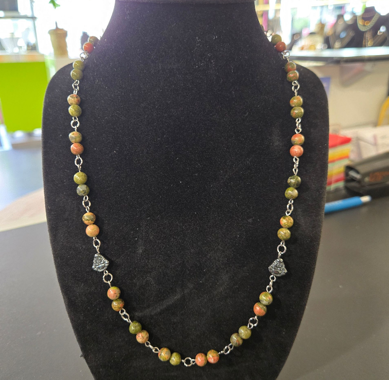 Collier de perles orné de pierres multicolores, présenté sur un support en forme de buste.