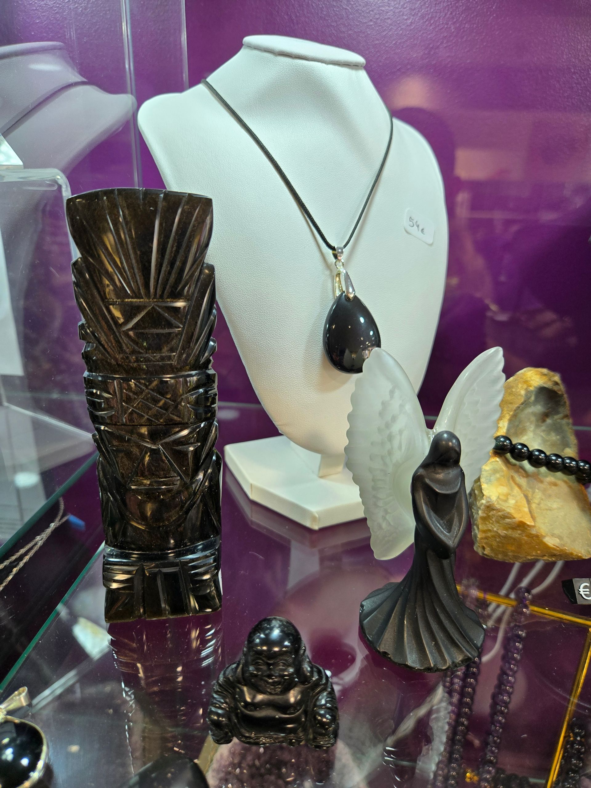 Vitrine présentant un buste orné d'un collier et plusieurs sculptures de pierres précieuses sur une surface réfléchissante.