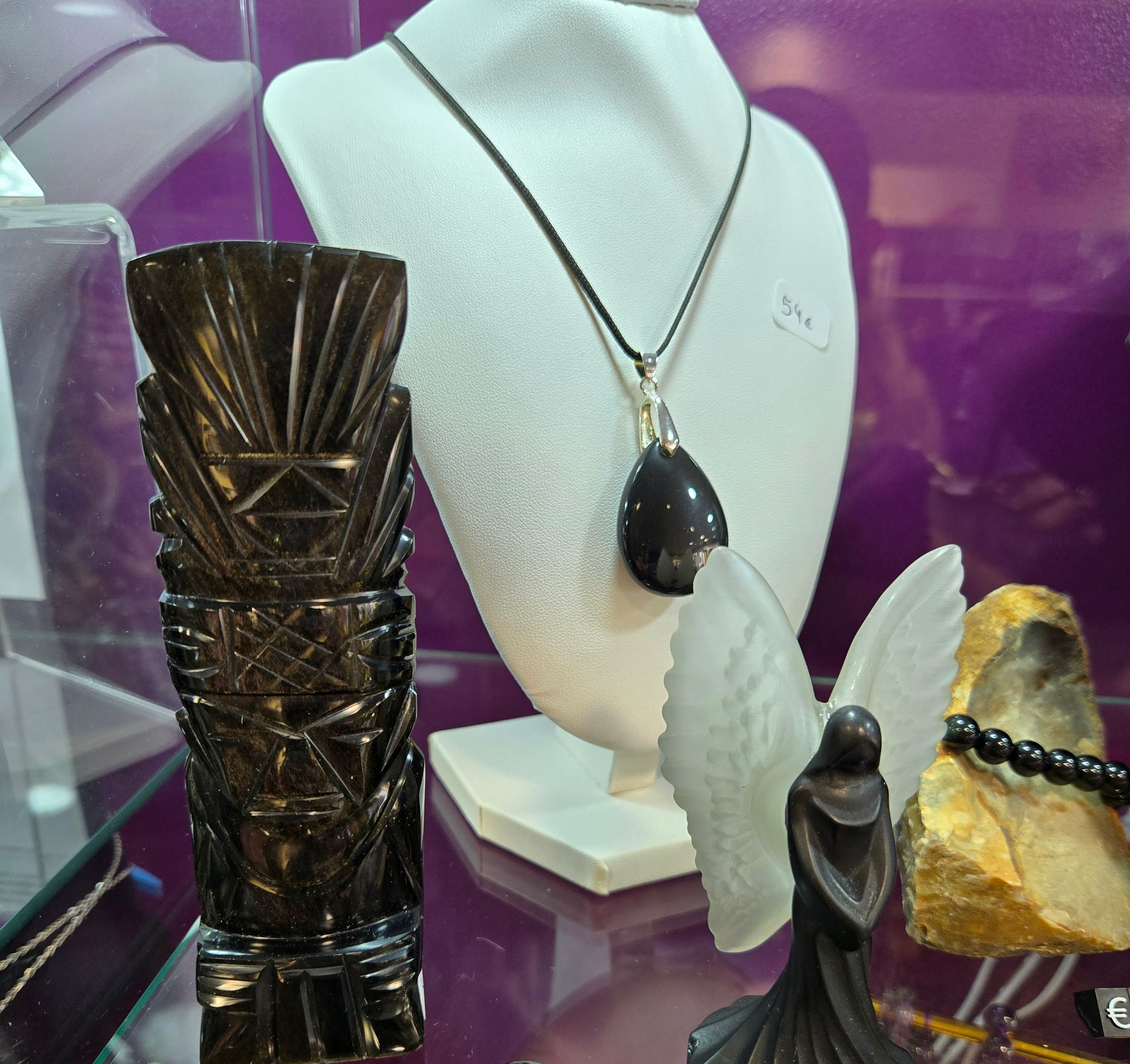 Présentoir à bijoux comprenant un buste, un collier en pendentif, un totem en bois sculpté et de petites figurines en pierres précieuses.