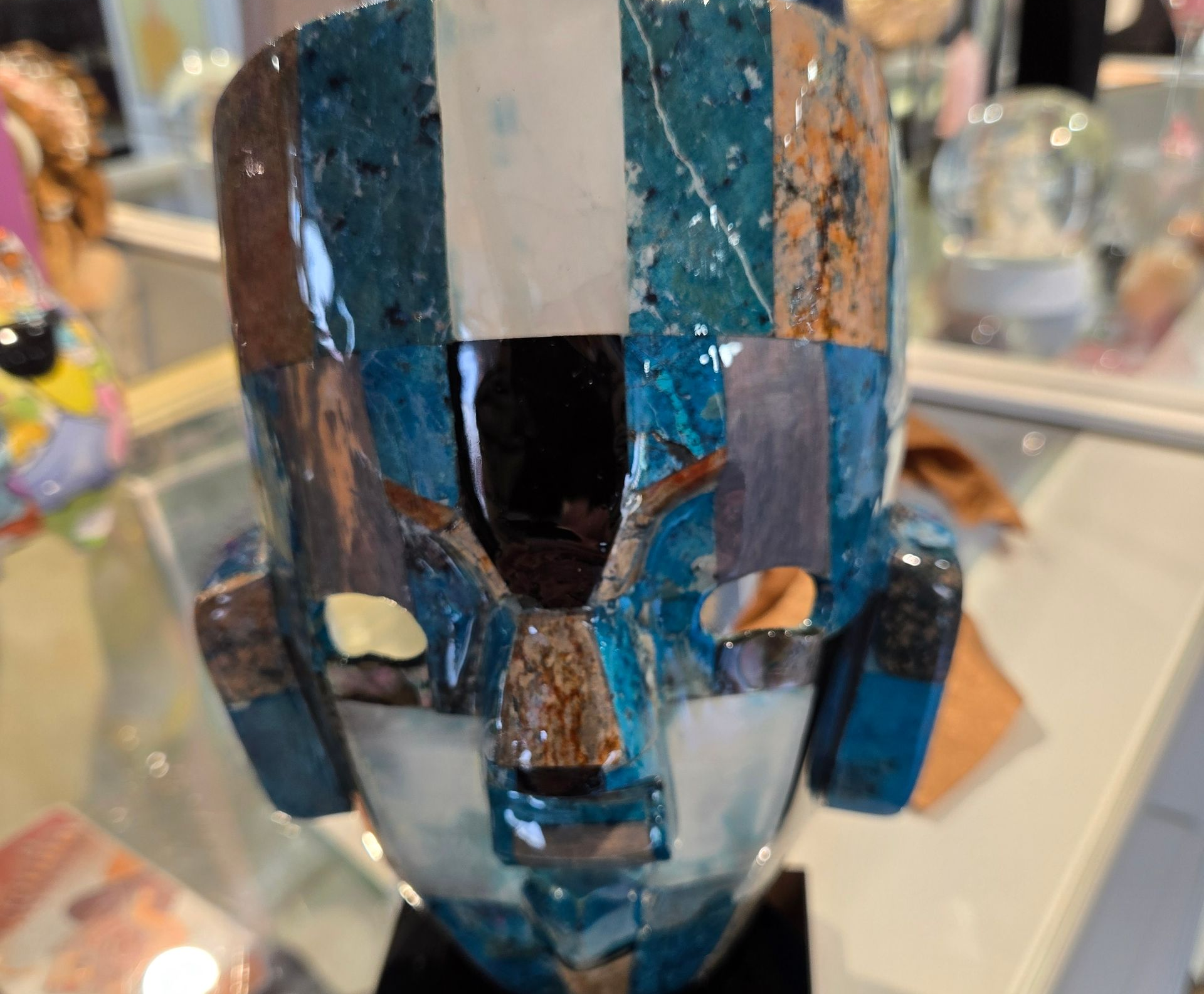 Sculpture de masque facial en mosaïque colorée sur un présentoir dans une galerie ou une boutique.
