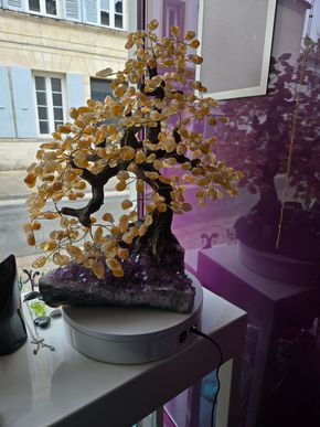 Sculpture décorative de bonsaï à feuilles dorées posée sur une table près d'une fenêtre, avec des bâtiments à l'extérieur.