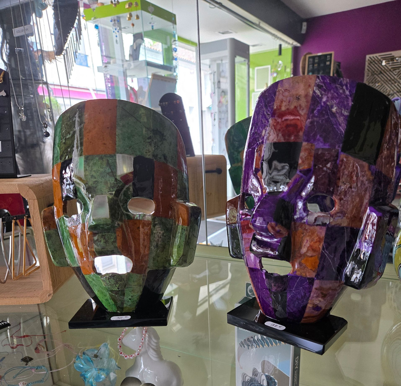 Deux sculptures de visages en mosaïque colorée sont exposées sur des socles dans une vitrine.
