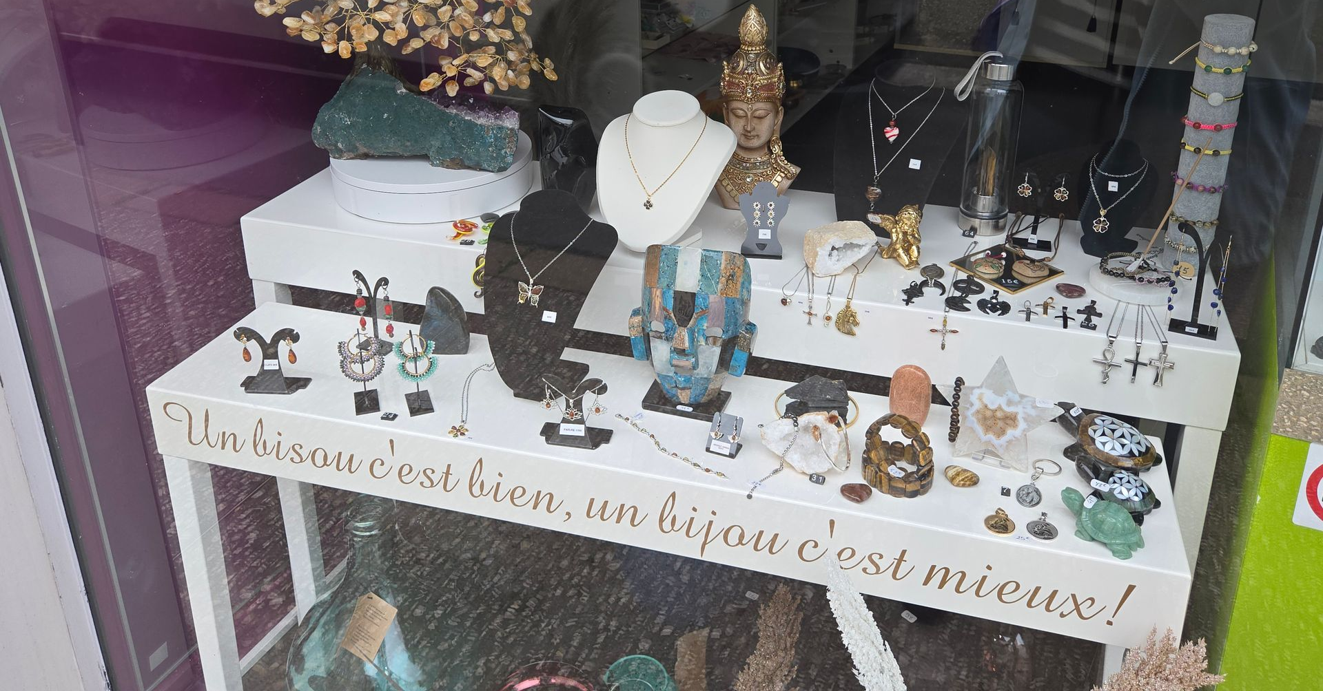 Vitrine d'un village de Noël miniature avec neige, sapins, figurines et une pancarte manuscrite.