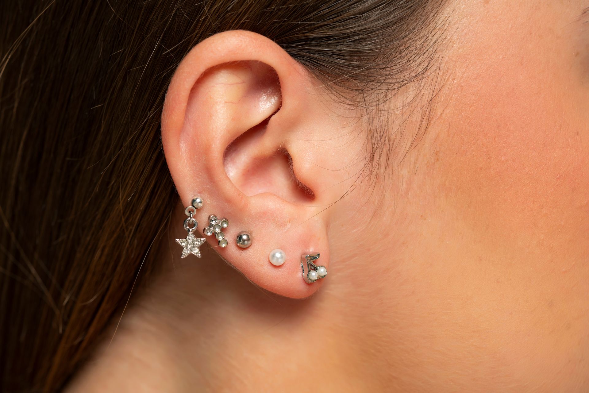 Gros plan sur une oreille ornée de plusieurs boucles d'oreilles argentées en forme d'étoile et de clous, contrastant avec des cheveux et une peau.
