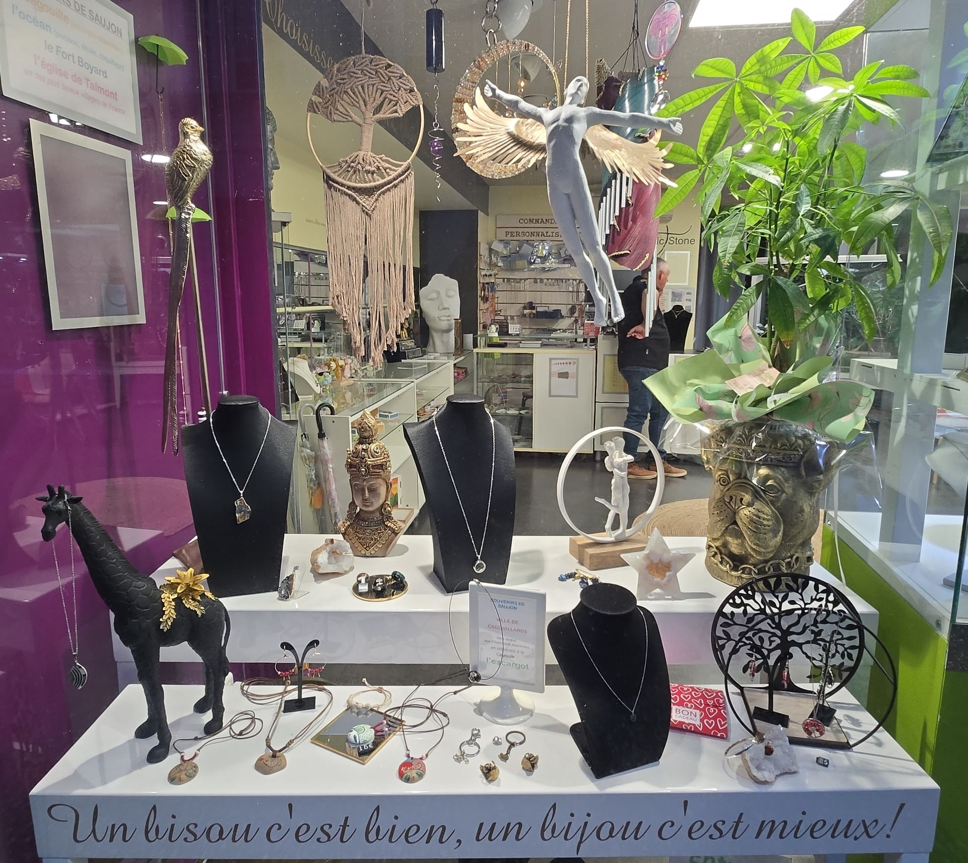 Présentation de bijoux et d'objets artisanaux dans une vitrine : colliers, bracelets et plante en pot.