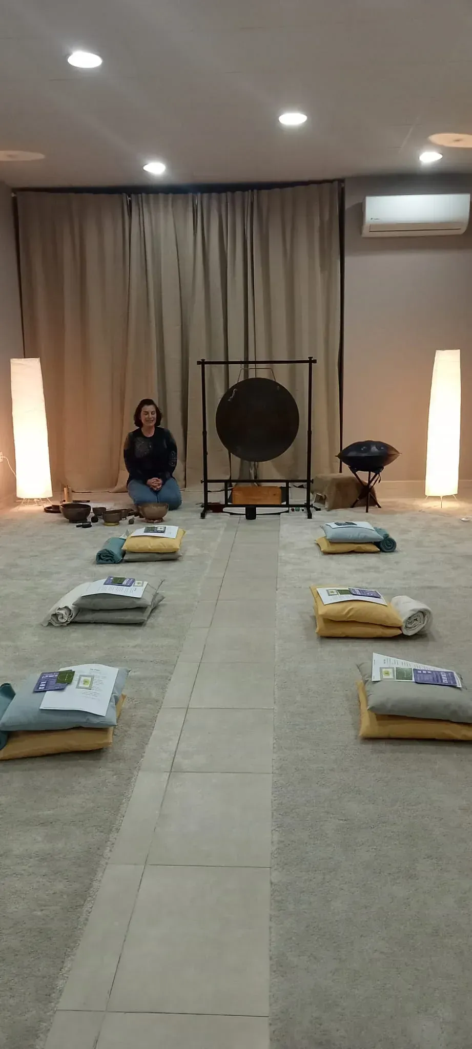 Una mujer está sentada en el suelo en una habitación con un gong de fondo.