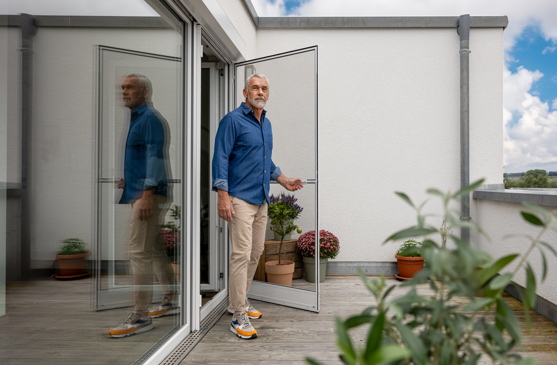Ein Mann steht in den offenen Flügeltüren Ein Mann tritt durch eine offene Glastür auf eine Terrasse; Drehrahmen
