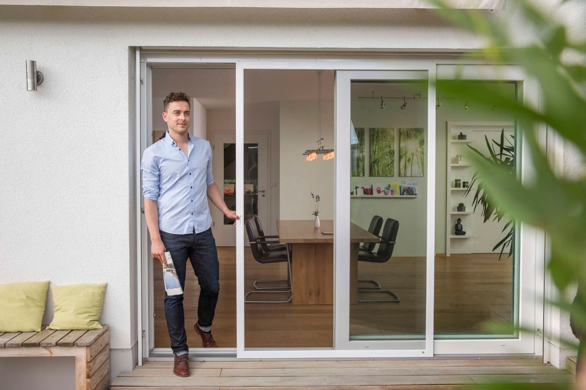 Ein Mann steht im Türrahmen zu einer Terrasse mit Glasschiebetüren und Sitzgelegenheiten im Freien.