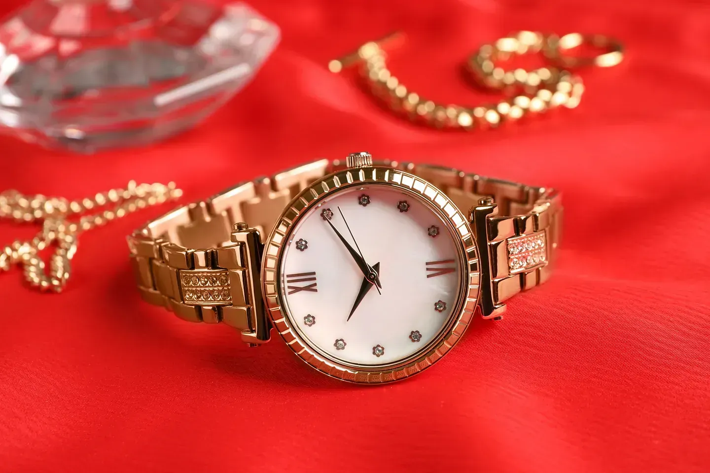Un reloj de oro reposa sobre un paño rojo al lado de unas joyas.