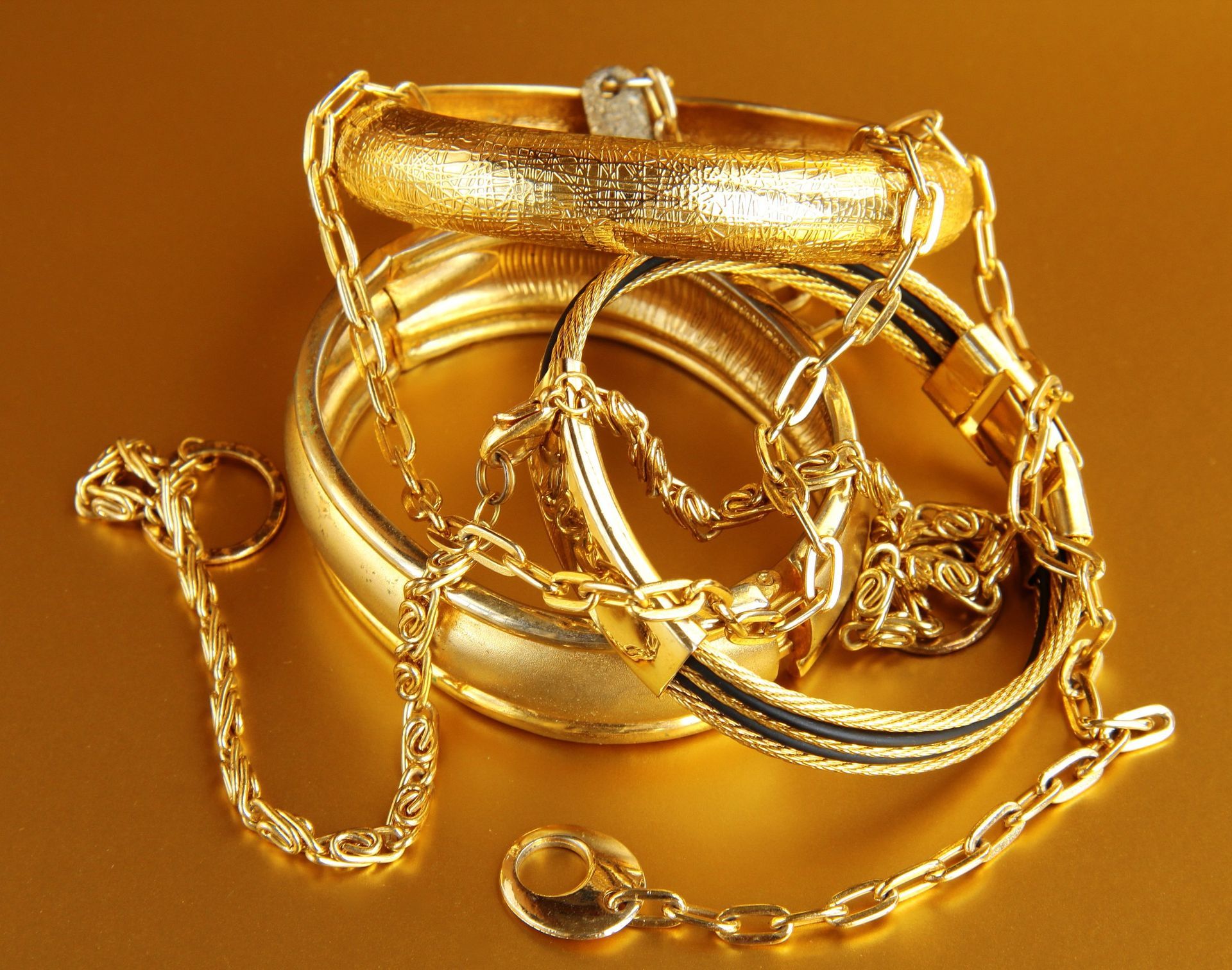 Una pila de pulseras y cadenas de oro sobre una superficie dorada.