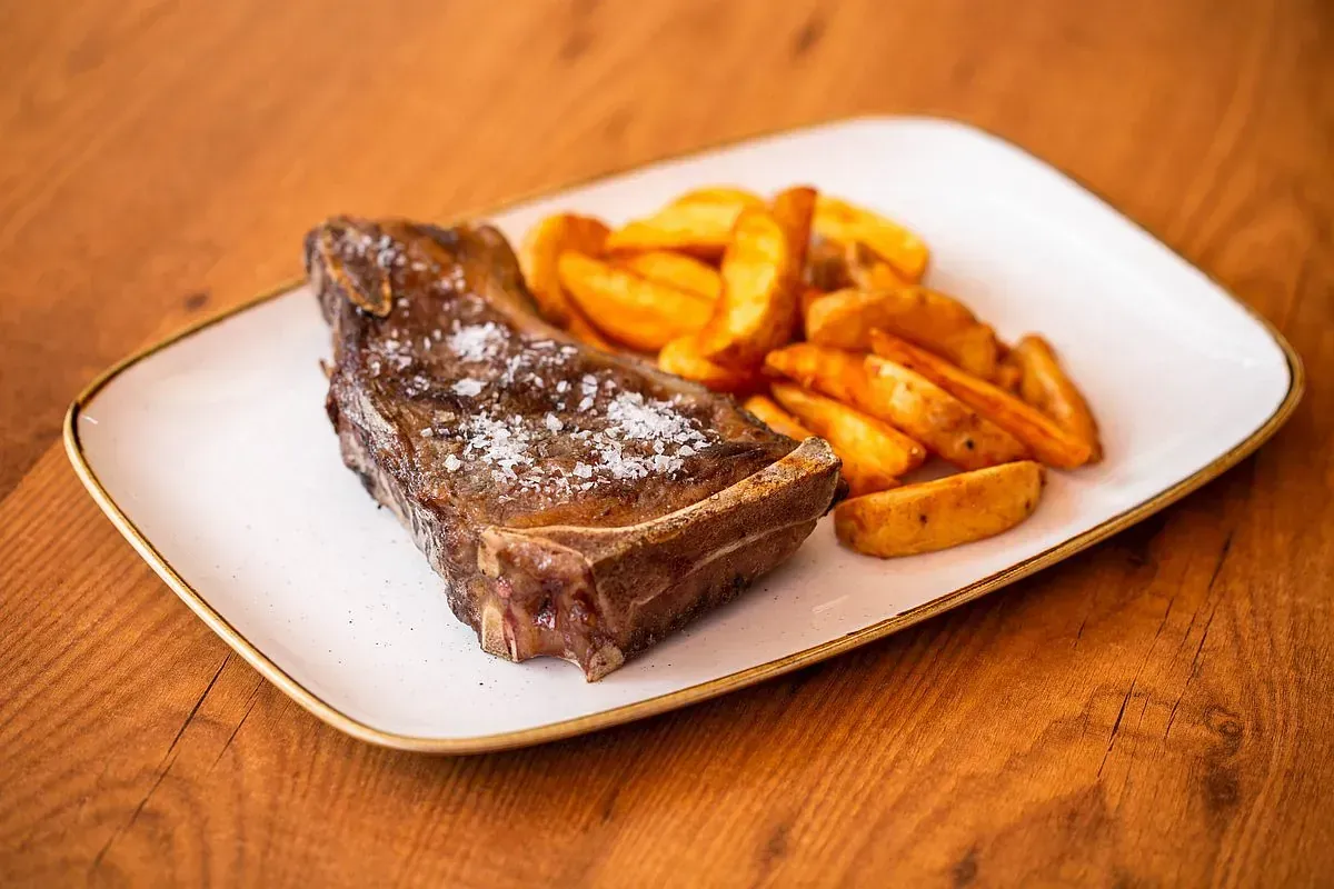 Filete con sal gruesa y gajos de patata sazonados en un plato blanco, mesa de madera.