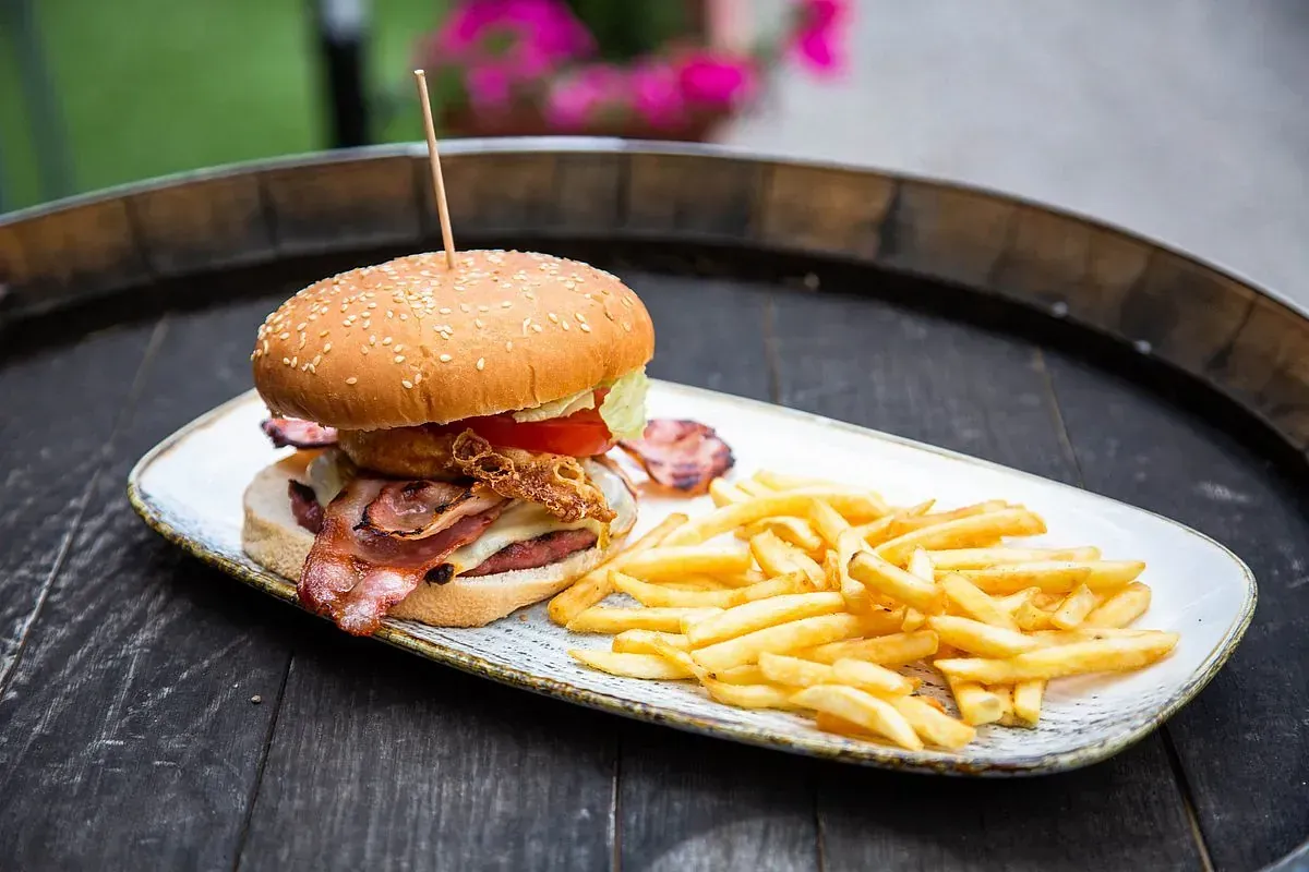 Hamburguesa con tocino, aros de cebolla y papas fritas en un plato sobre un barril de madera.