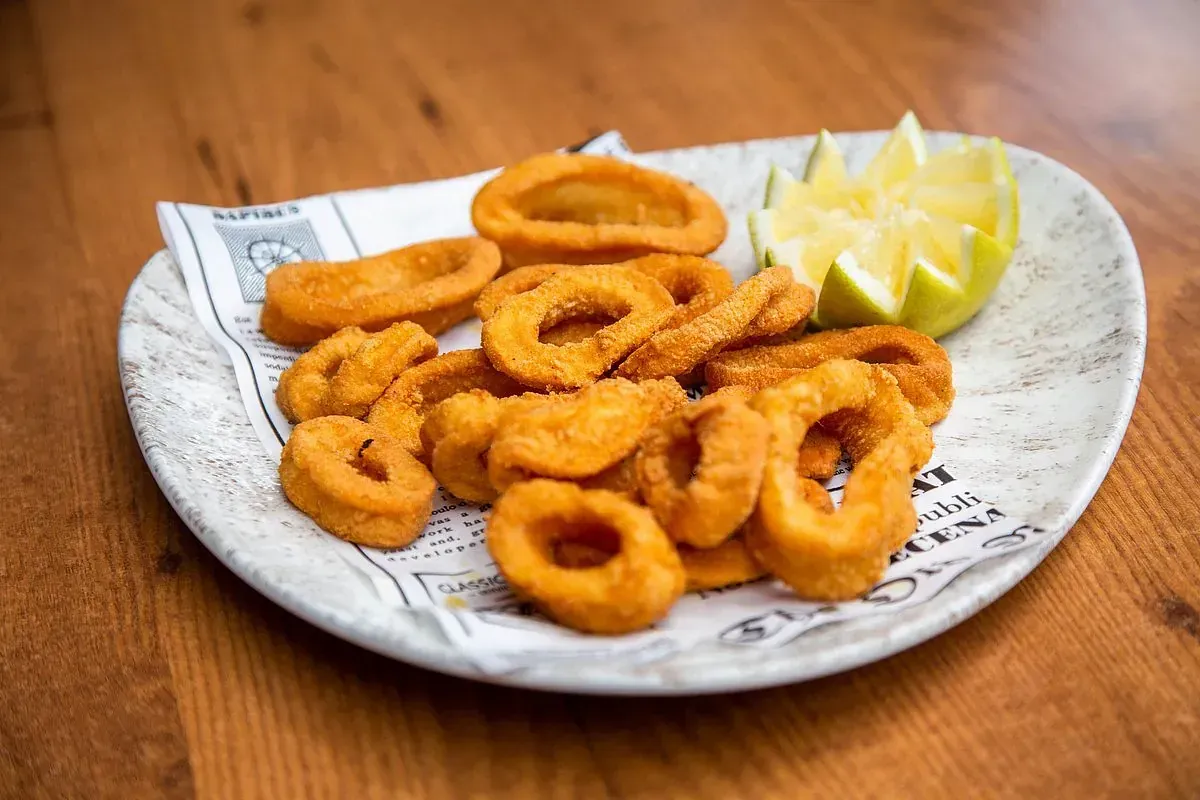 Plato de aros de calamar fritos con una rodaja de limón sobre una mesa de madera.