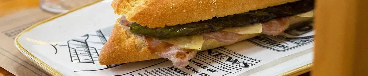 Sándwich cubano en un plato decorativo, compuesto de pan, jamón, queso y un pepinillo.