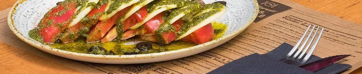 Ensalada caprese con pesto en un plato moteado, con tenedor y servilleta aparte.