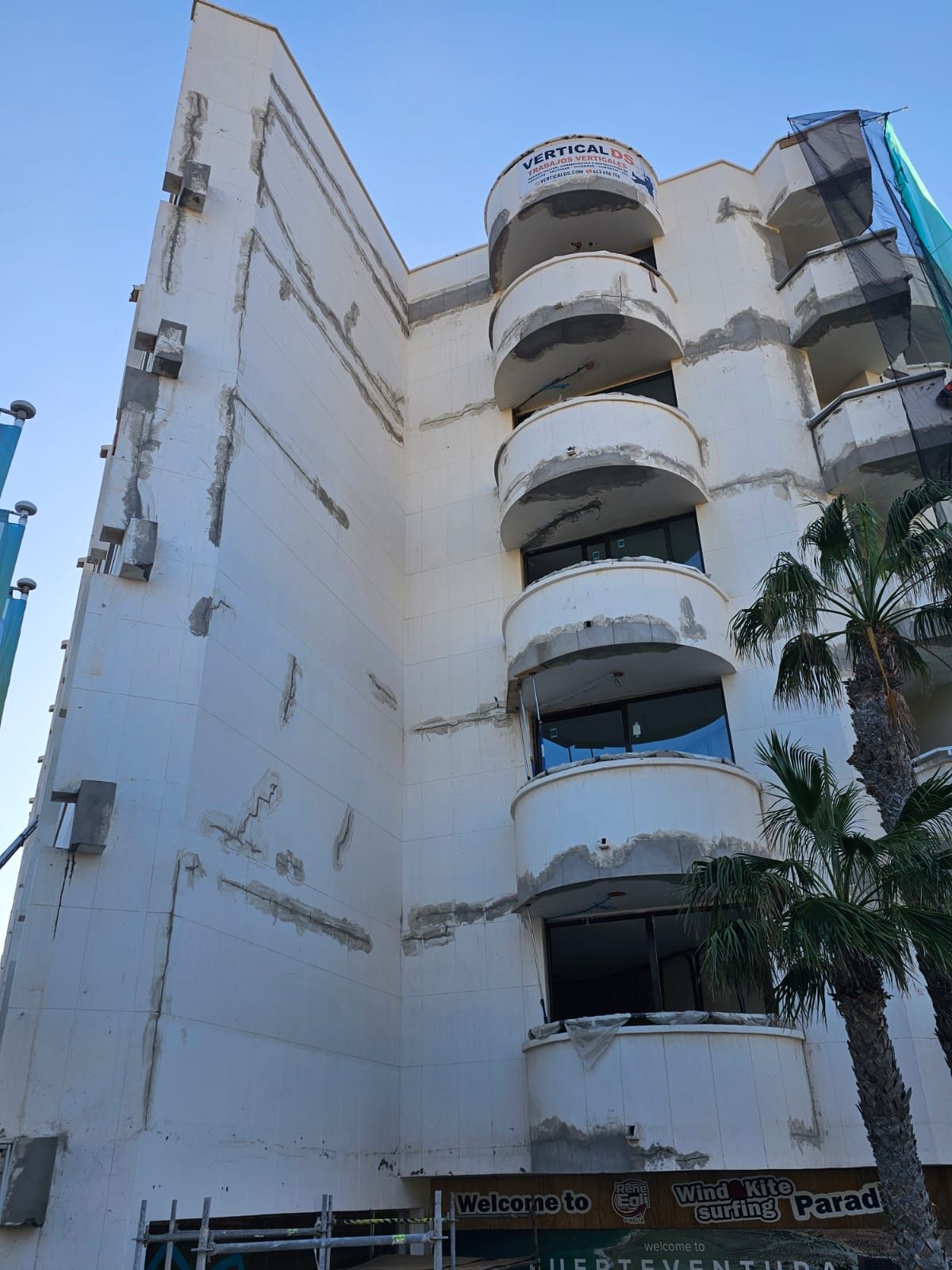 Un gran edificio blanco con balcones y una palmera delante.