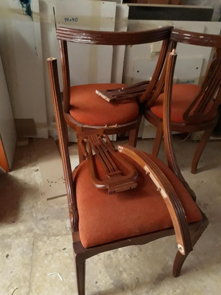 Silla de madera rota con cojín naranja y piezas del respaldo desprendidas, en el interior.