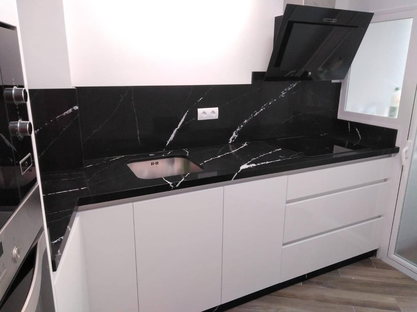 Cocina moderna con encimera de mármol negro y gabinetes blancos.