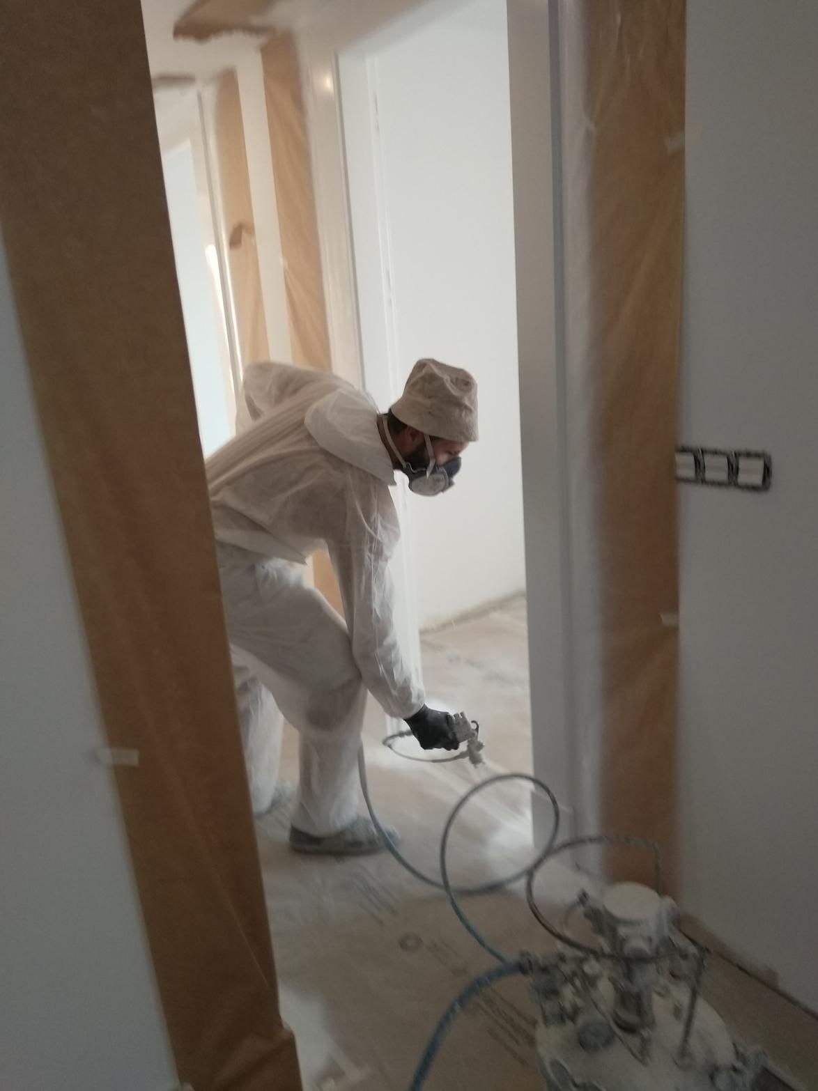 Una persona con traje de protección rocía pintura dentro de una habitación.