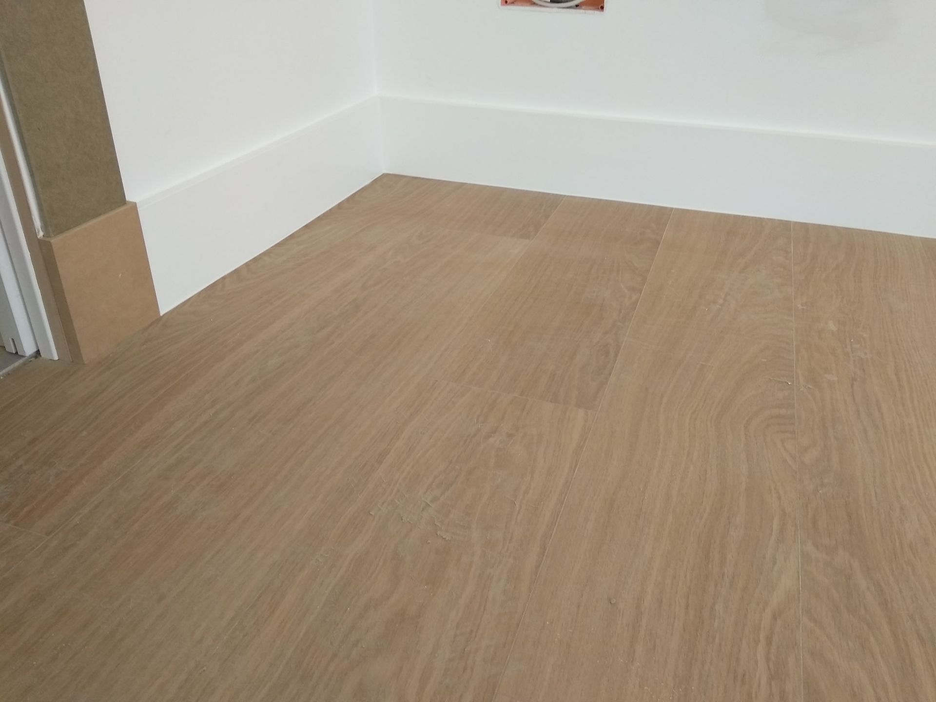 El piso de madera clara combina con el zócalo blanco y la esquina de la pared.