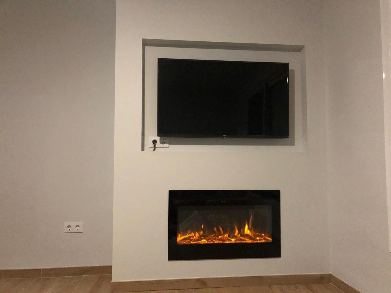 Televisor montado encima de una chimenea eléctrica empotrada en una pared blanca.