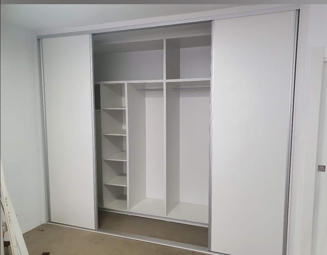 Armario de puertas correderas blancas con estantes y espacio para colgar.