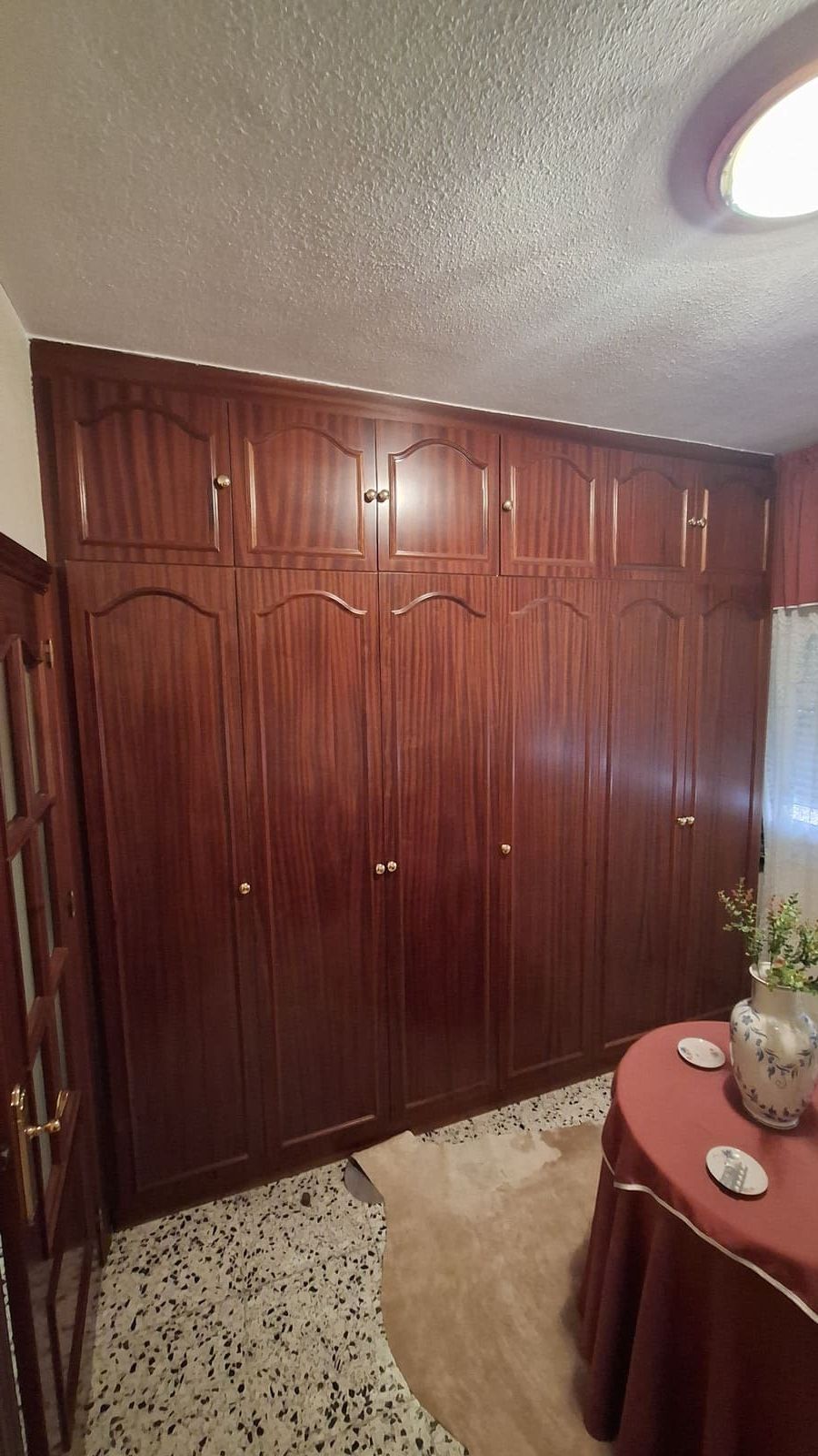 Armario de madera oscura con múltiples puertas en una habitación con piso estampado.