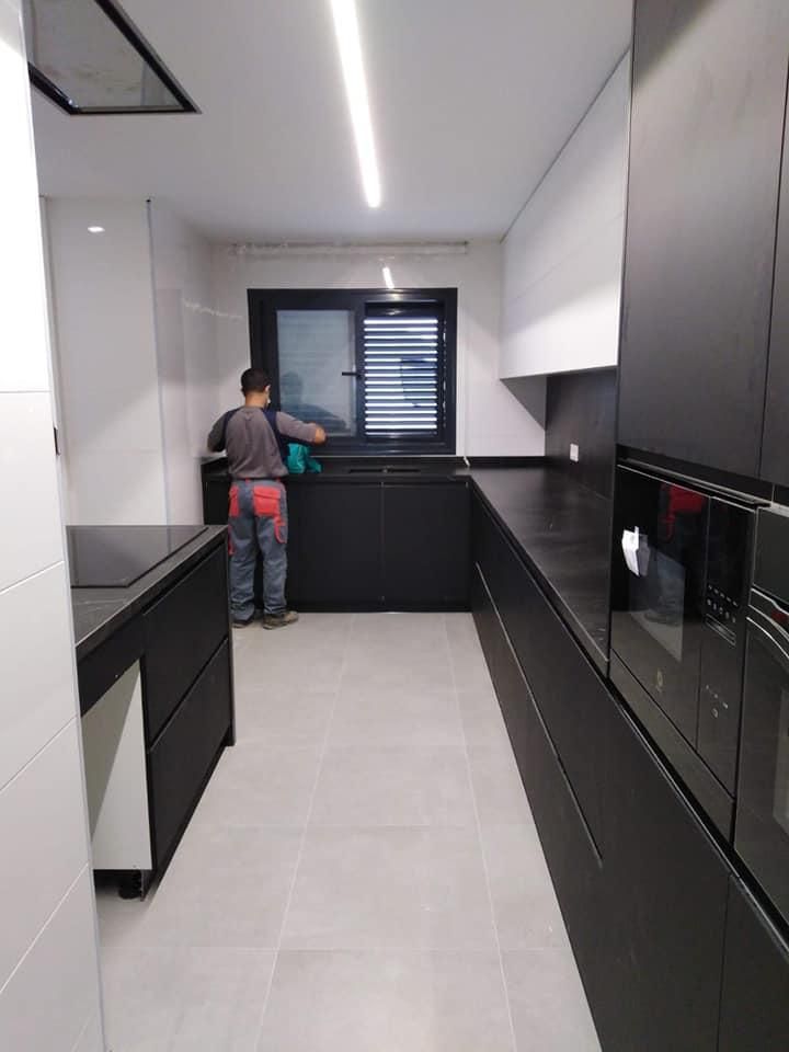 Una persona limpia una cocina oscura con armarios y electrodomésticos negros. Hay una ventana en el centro de la habitación.