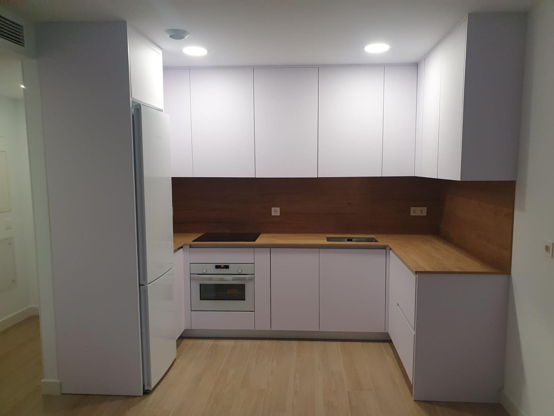 Cocina moderna blanca con encimera y protector contra salpicaduras de madera clara.