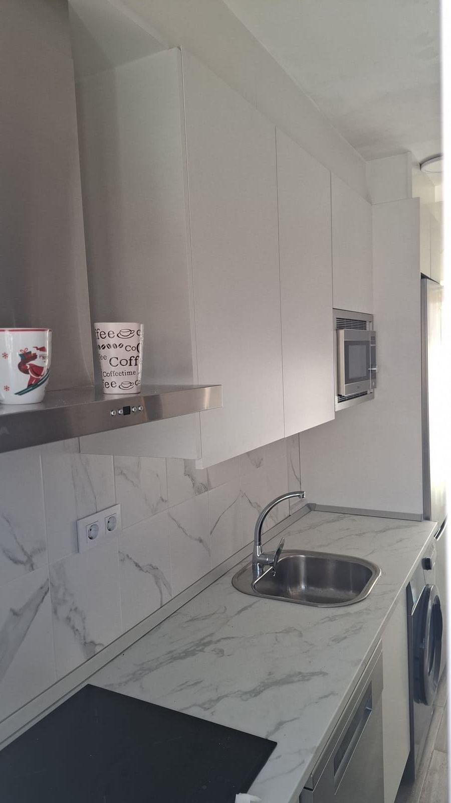 Cocina moderna con gabinetes blancos, salpicadero y encimeras de mármol y electrodomésticos de acero inoxidable.