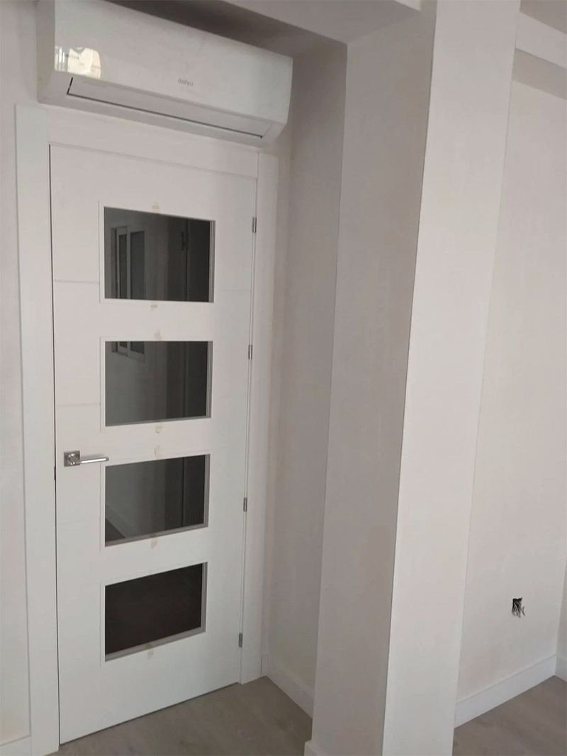 Puerta blanca con paneles de vidrio y unidad de aire acondicionado encima.