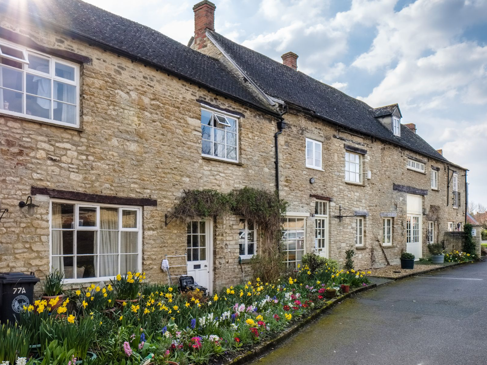 Rangée de maisons en pierre avec des fleurs devant ; journée ensoleillée.
