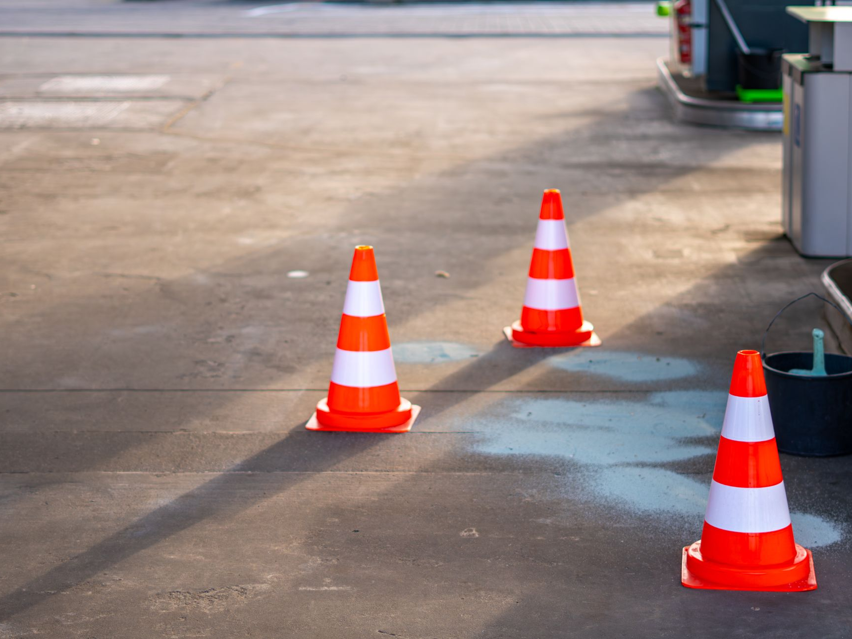 Trois cônes de signalisation orange et blancs sur une surface en béton d'une station-service.