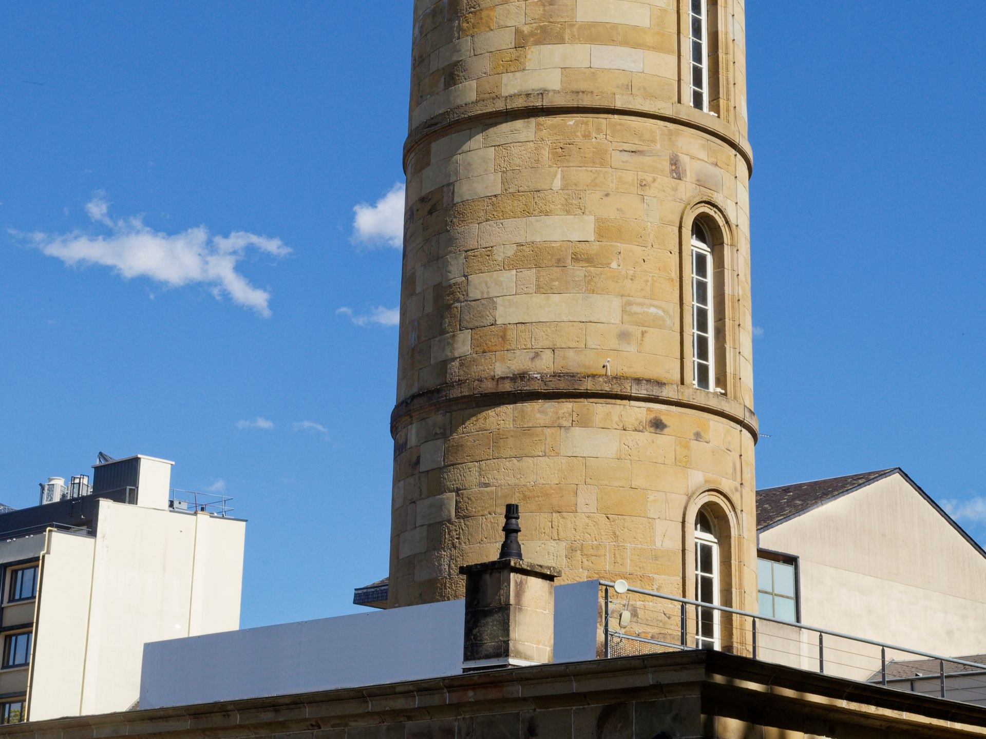 Tour de pierre aux fenêtres cintrées, se détachant sur un ciel bleu nuageux.