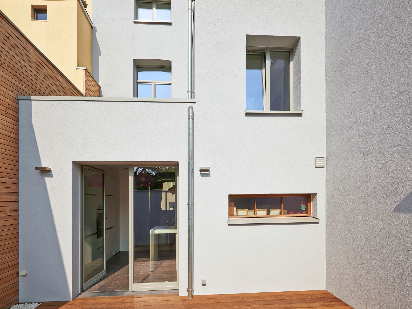 Vue extérieure d'un bâtiment blanc avec une porte vitrée, des fenêtres et une terrasse en bois.