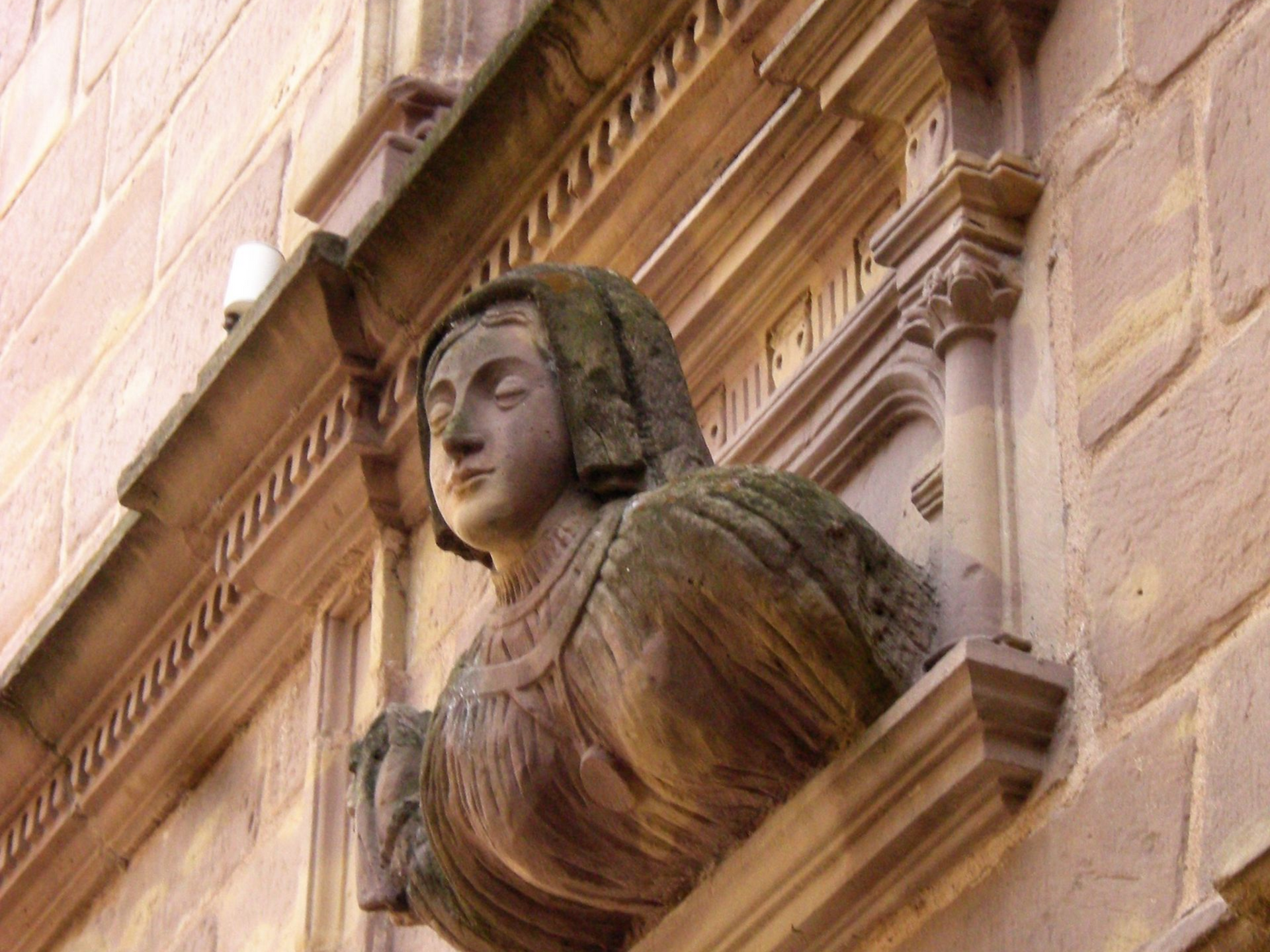 Sculpture en pierre représentant une femme, encastrée dans la façade extérieure d'un bâtiment.