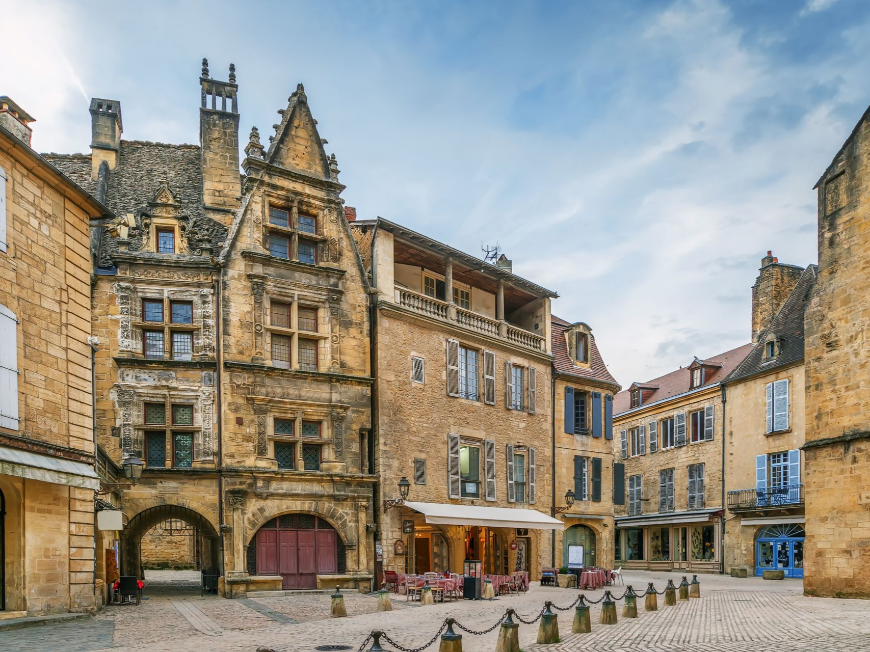 Place pavée à Sarlat, en France, avec des bâtiments médiévaux couleur sable et des terrasses de café.