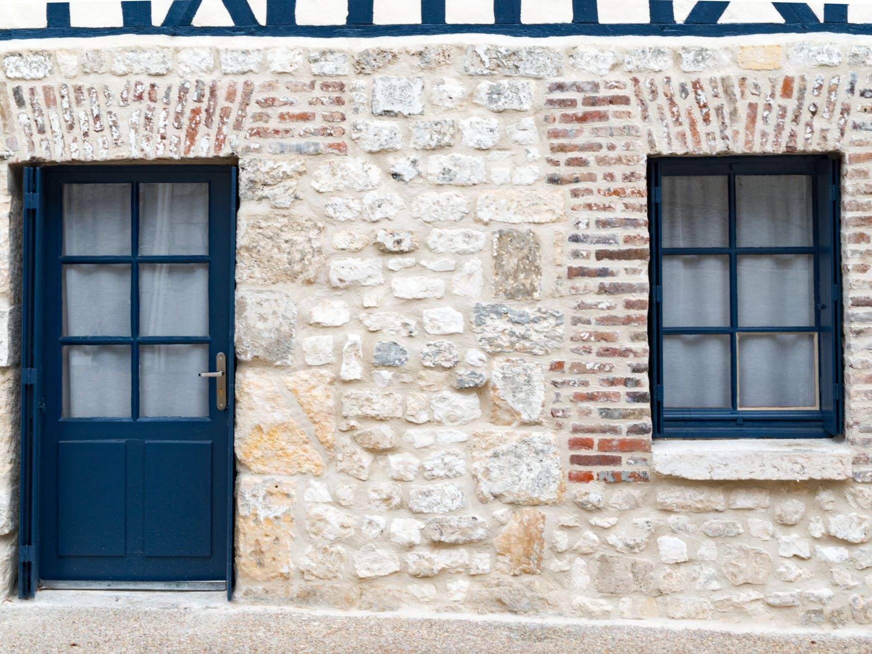 Porte et fenêtre bleues sur un bâtiment en pierre et en brique ; encadrements blancs et détails bleus sur le toit.
