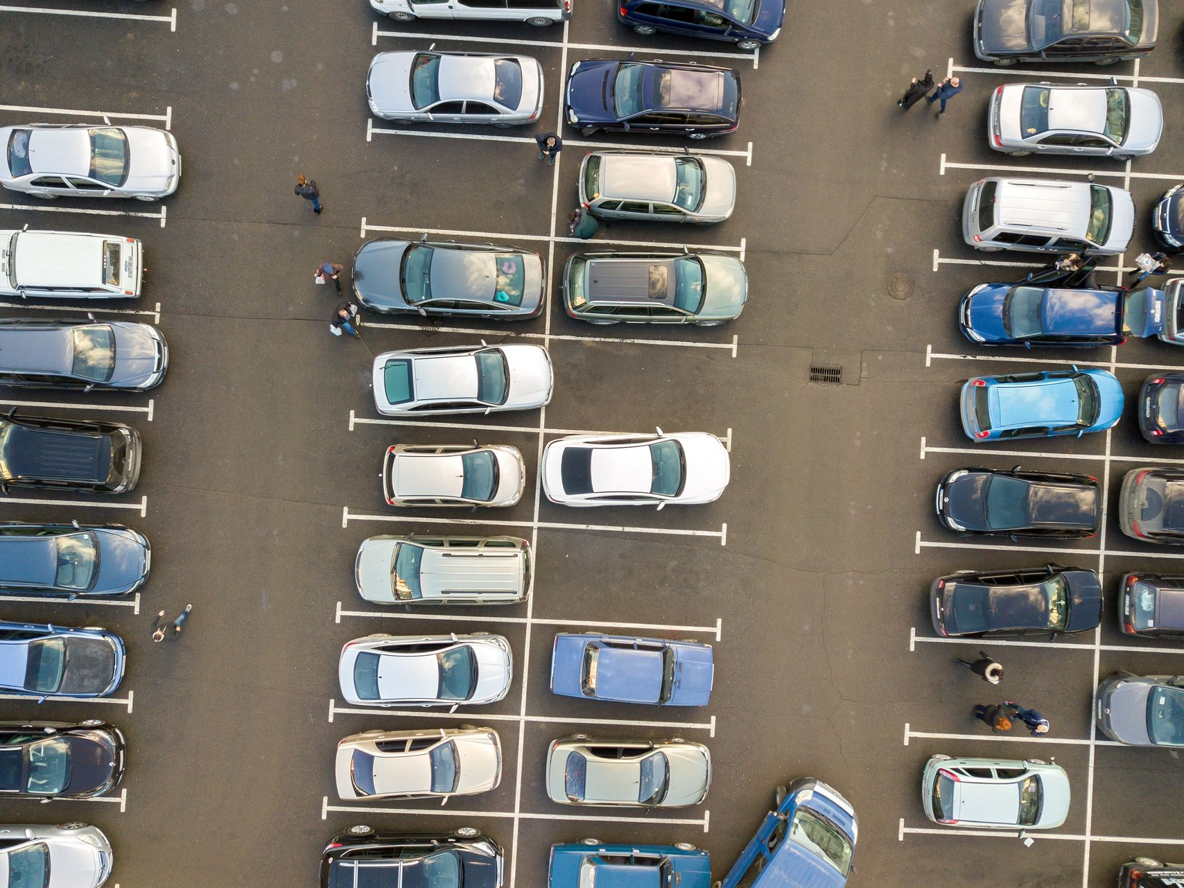 Vue aérienne d'un parking rempli de voitures ; plusieurs personnes se promènent.
