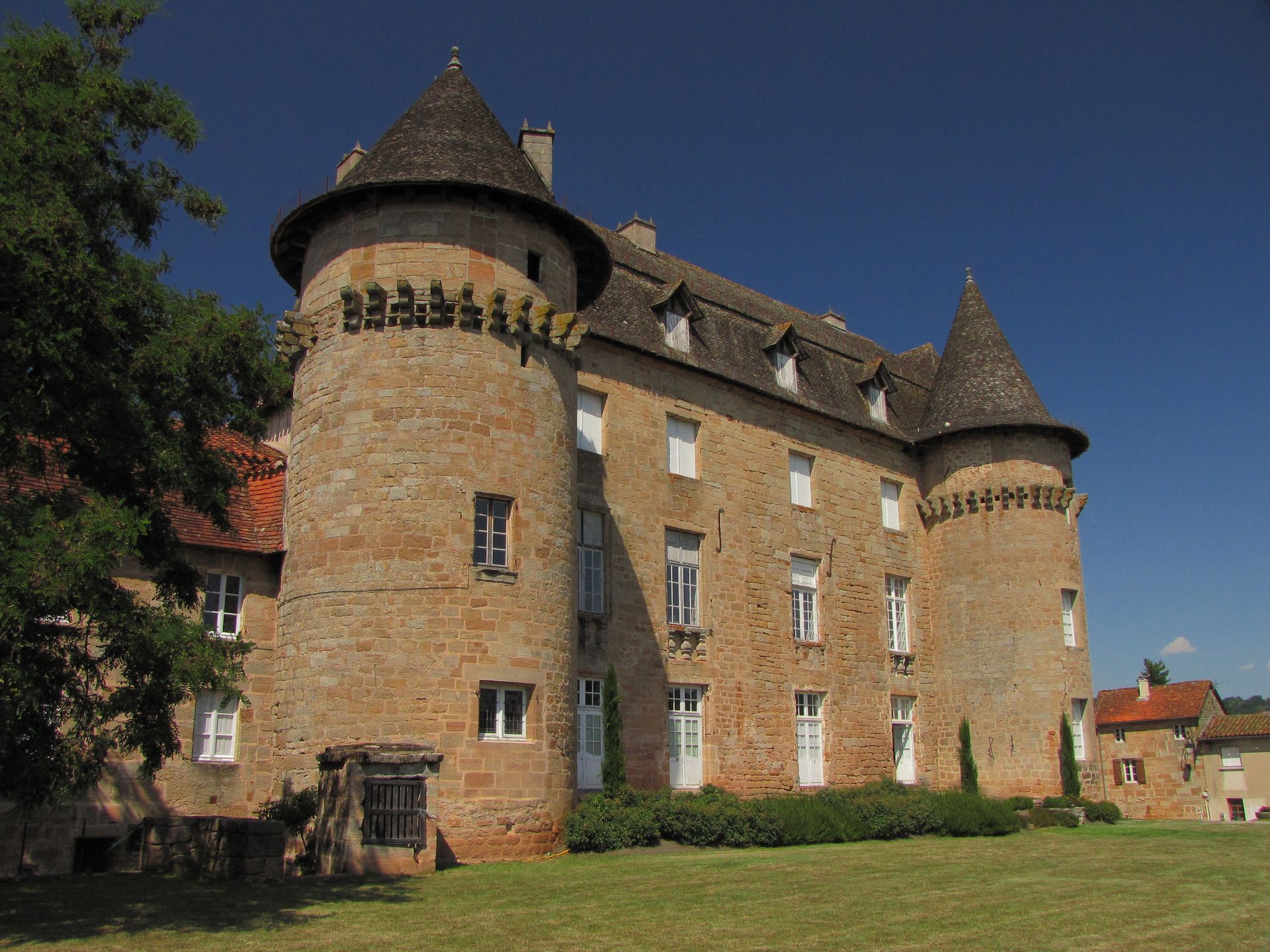 Château de pierre avec deux grandes tours cylindriques, situé sur une pelouse verdoyante sous un ciel d'un bleu limpide.