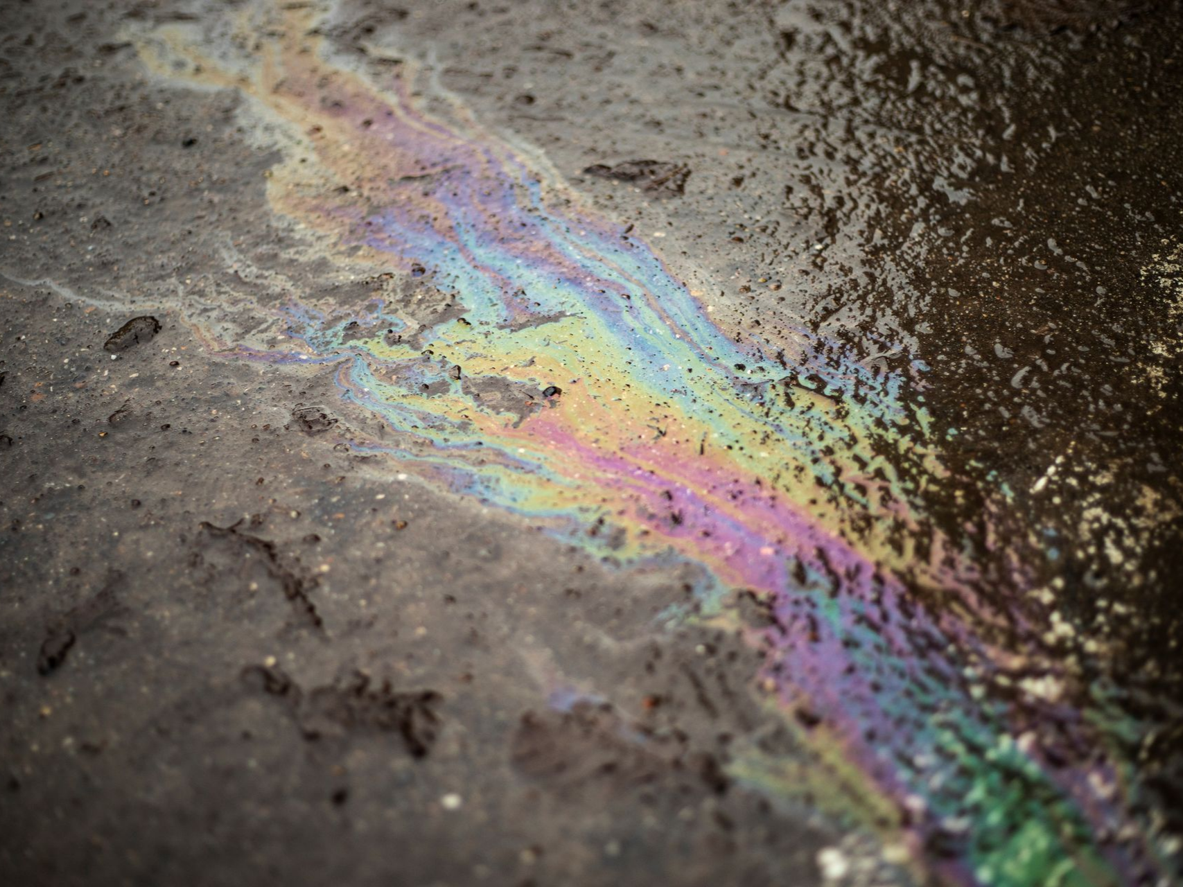 Nappe d'huile irisée sur l'asphalte mouillé, reflétant les couleurs de l'arc-en-ciel.