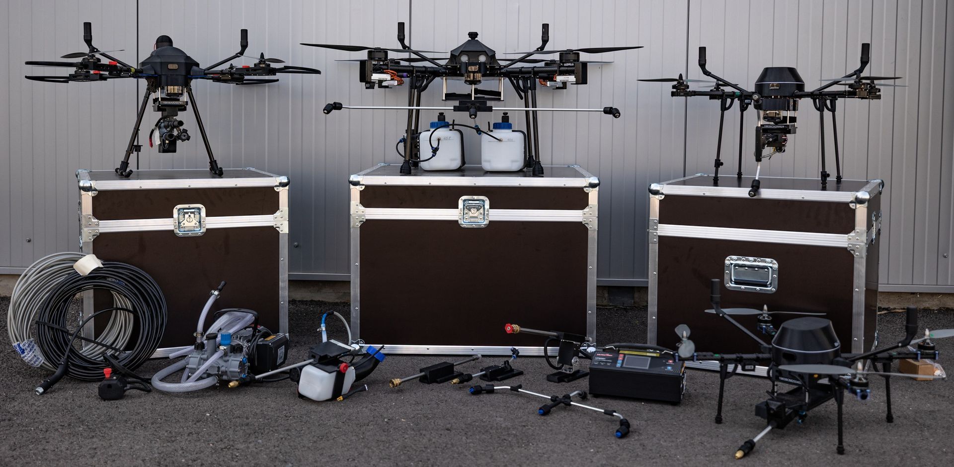 Trois gros drones sont exposés sur des caisses, avec du matériel supplémentaire au sol devant eux.