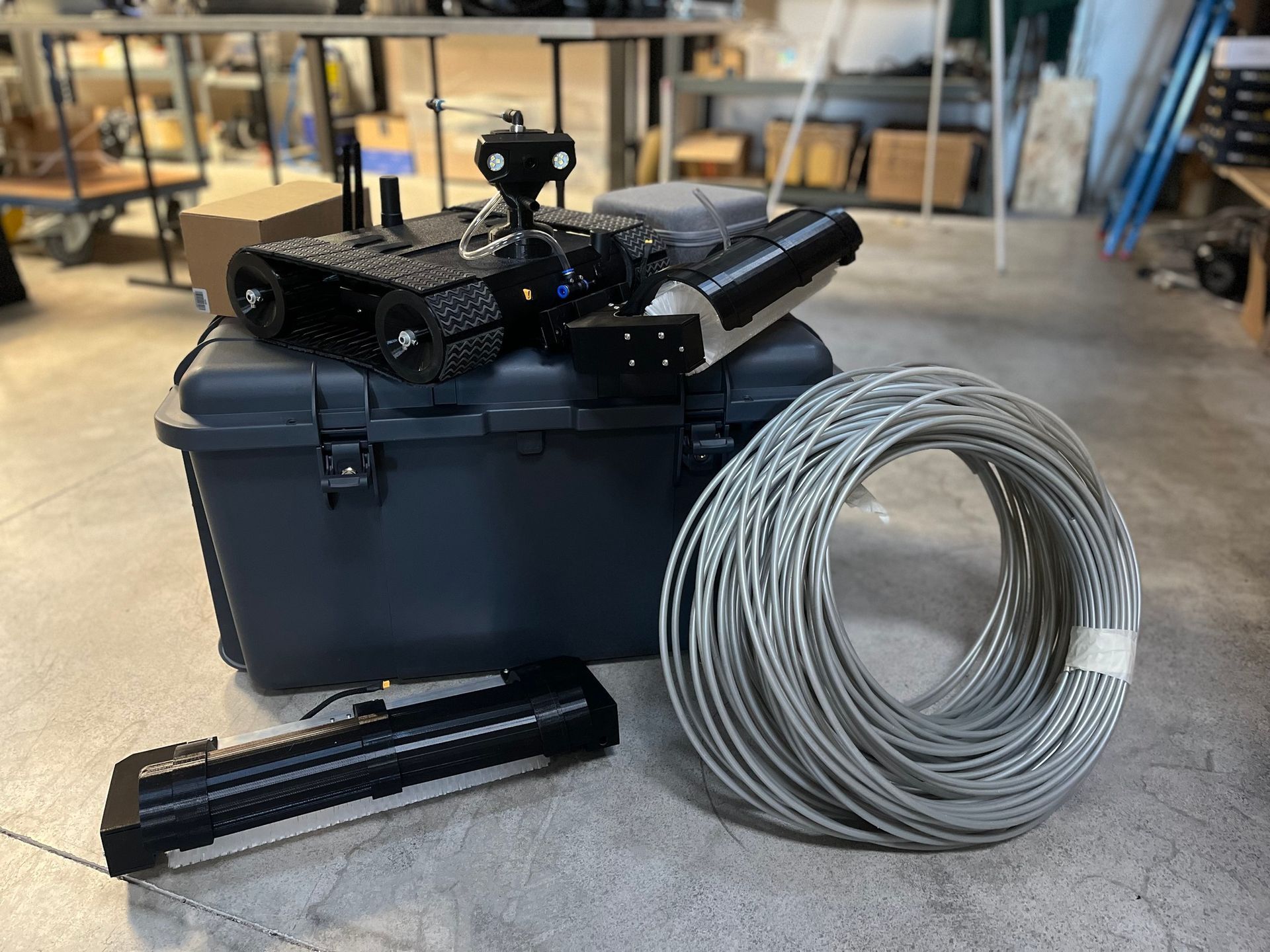 Robot noir sur une mallette contenant des câbles enroulés et d'autres équipements.