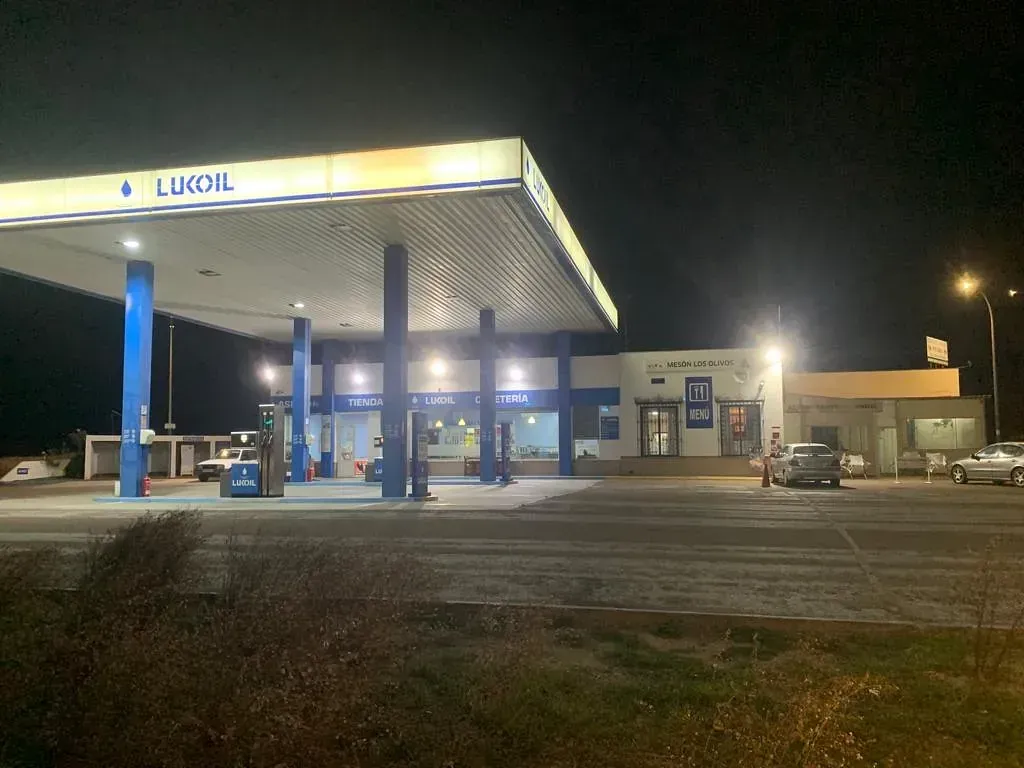 Una gasolinera está iluminada por la noche con coches aparcados delante de ella.