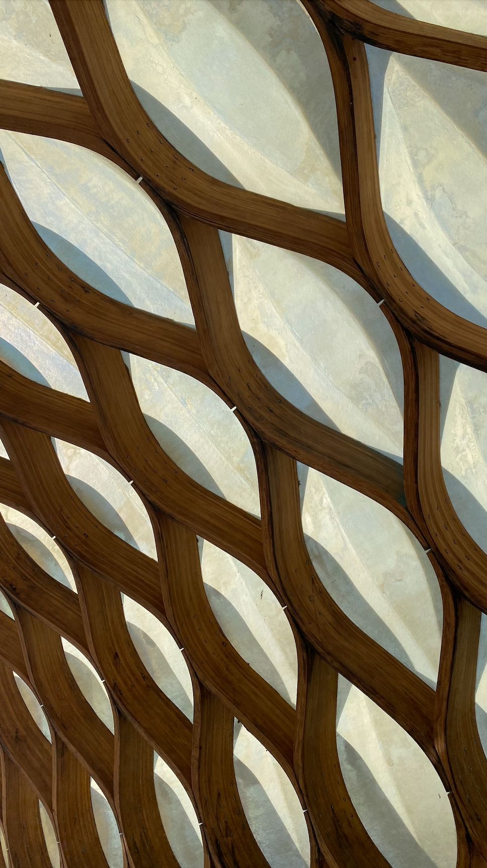 Enrejado de madera entrelazado sobre una superficie translúcida, creando un patrón texturizado con sombras.