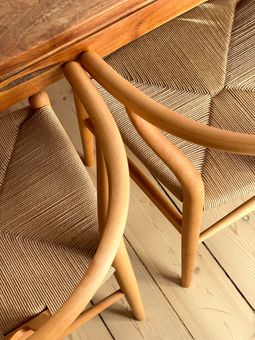 Sillas de madera con asientos de mimbre y patas curvas bajo una mesa de madera.