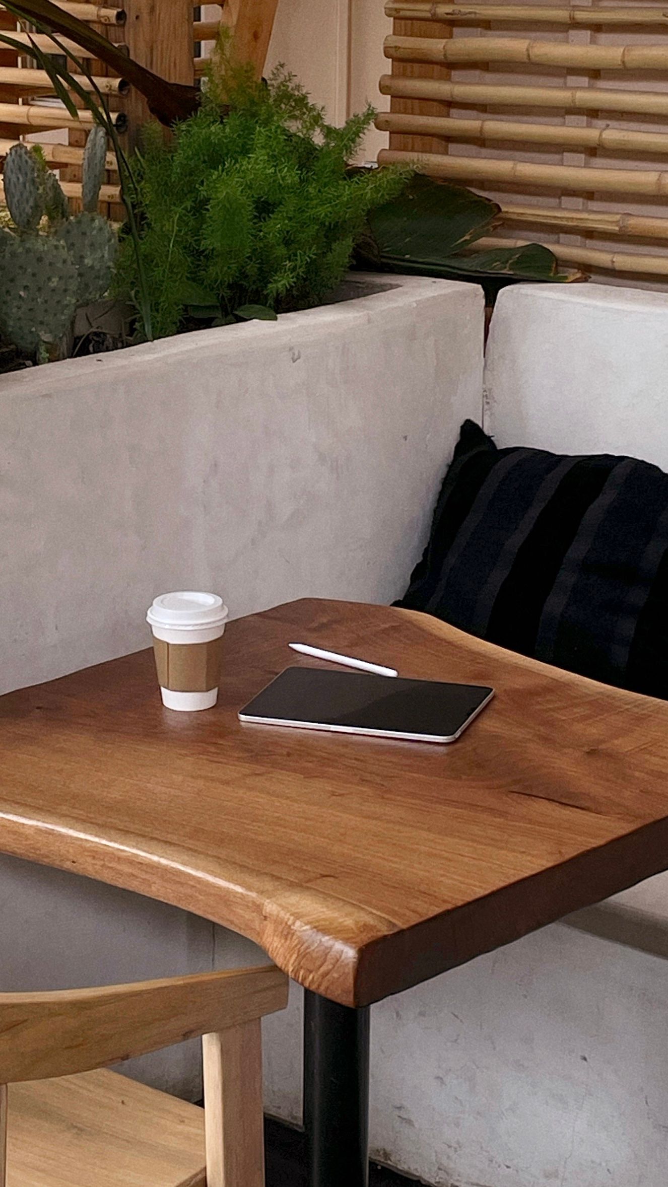 Mesa de madera en un ambiente de cafetería con una taza de café, una tableta y un cojín en un reservado.
